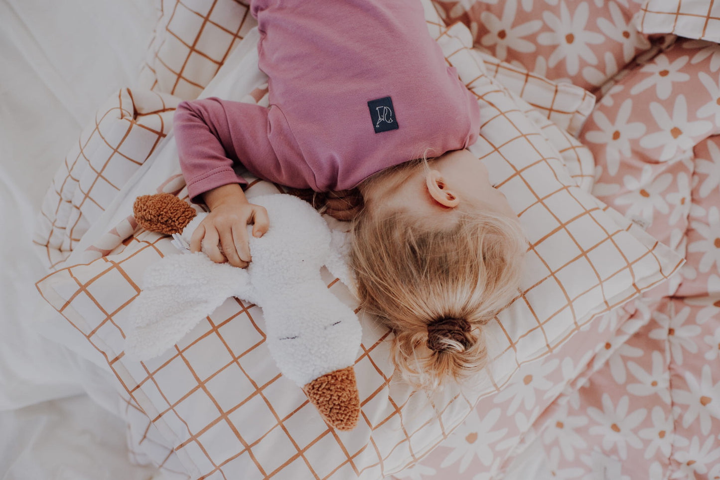 A child lying comfortably on a checkered camel-colored cotton bedding set while holding a white plush goose toy