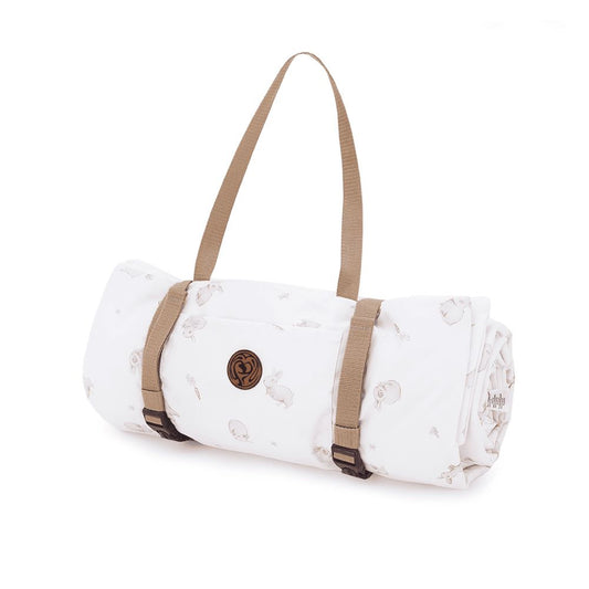 Opgerolde witte picknickmat met schattige konijnenprint, voorzien van beige draagbanden en een Makaszka-logo, perfect voor onderweg.
